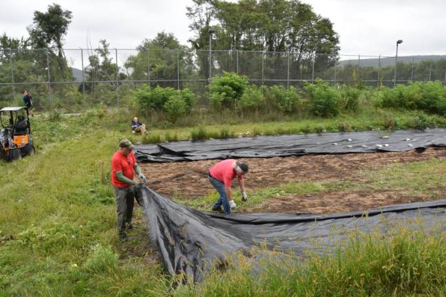 Greg Galluccio (left) and Jeff Zahn remove the tarps covering the future pollinator garden, while Geoff Howard looks on and Amy Sweetman takes photos in August.